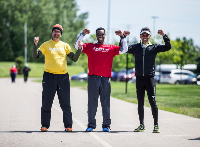 A smiling athlete and two volunteers flexing.