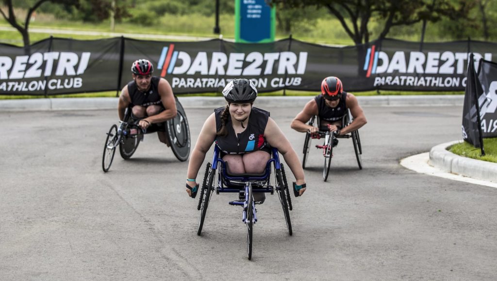 Three Dare2tri athletes in racing wheelchairs approach the finish line in unison.
