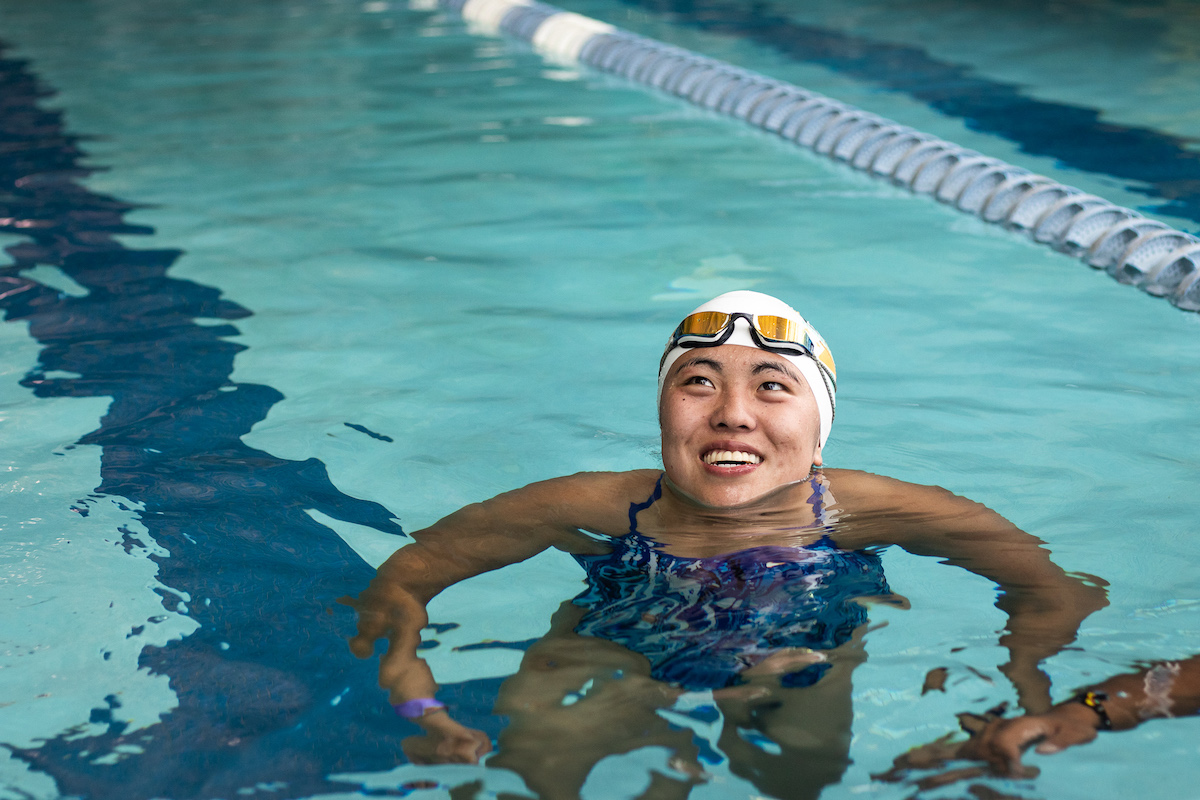 Jacie King swimming in an indoor pool wearing a swim cap and goggles on her forehead.
