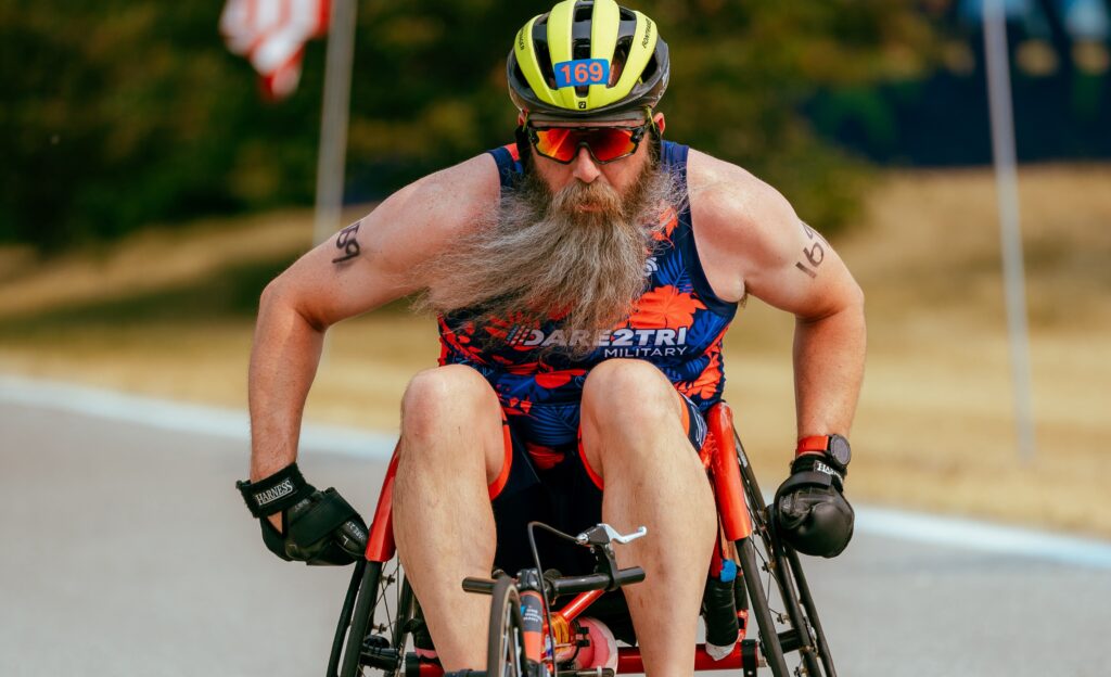 A bearded man pushing a racing chair outdoors.