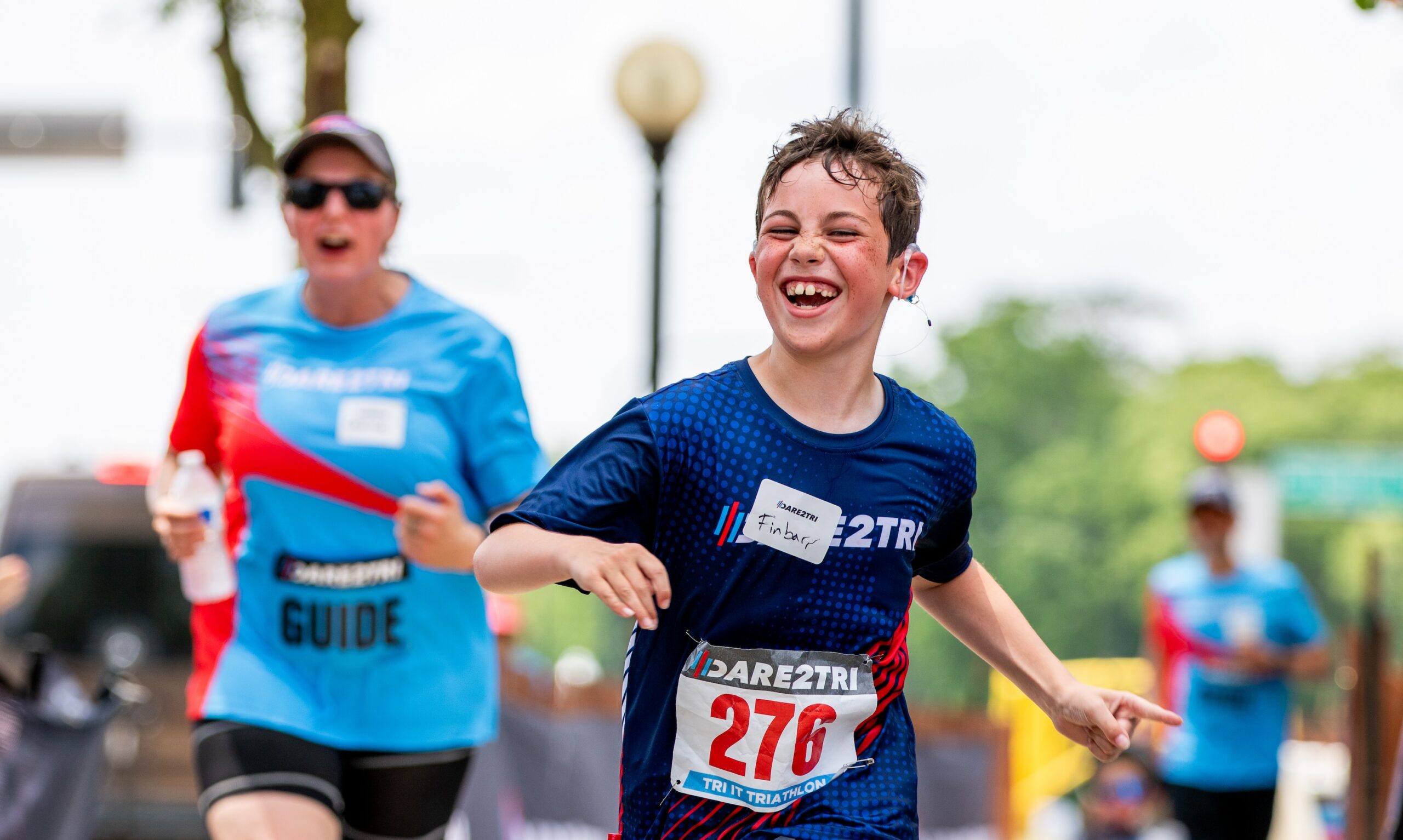Boy smiling and running with hearing device in one ear.